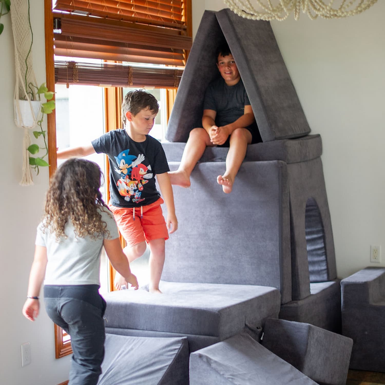 Three kids playing and climbing on a modular foam play couch for kids, building a tall floor couch fort—durable, Canadian-made, and perfect for indoor play.